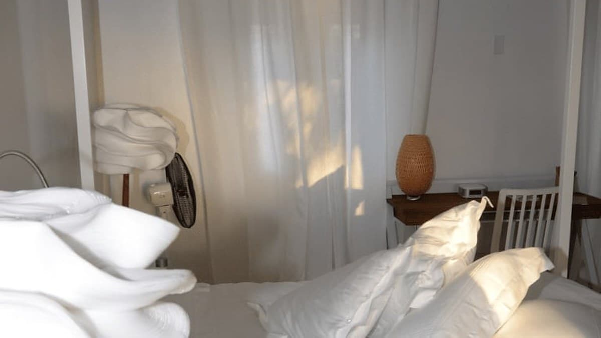Gyűrött ágynemű reggeli fényben, ventilátorral a falon